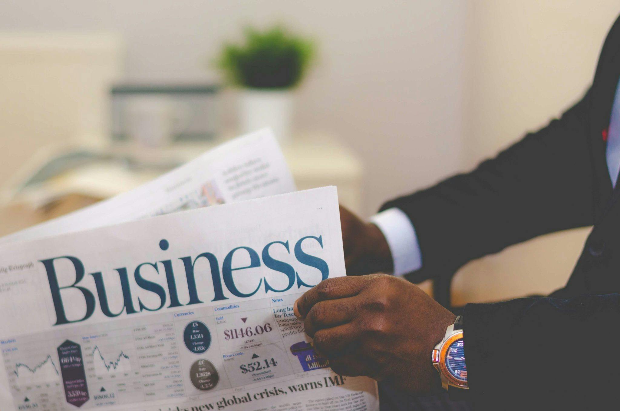 Close-up of a businessman reading a newspaper indoors, focusing on business headlines.